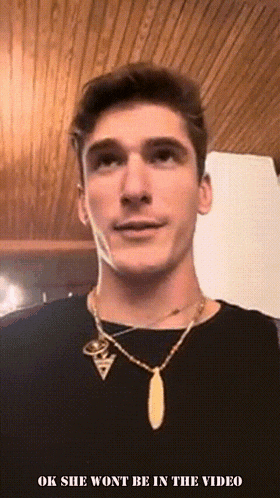a man wearing a necklace with the words ok she won 't be in the video below him