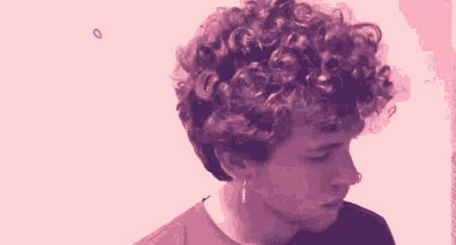 a young man with curly hair is wearing earrings and looking down .