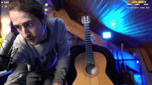 a man playing an acoustic guitar in front of a microphone with the words lista abierta on the screen behind him