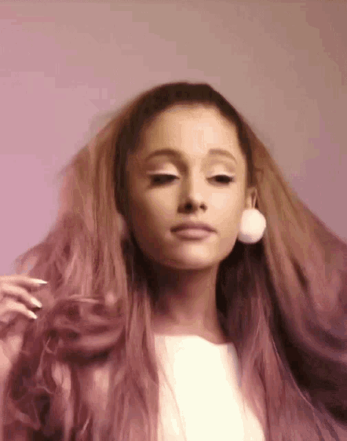 a woman with long pink hair is wearing a white shirt and white earrings .