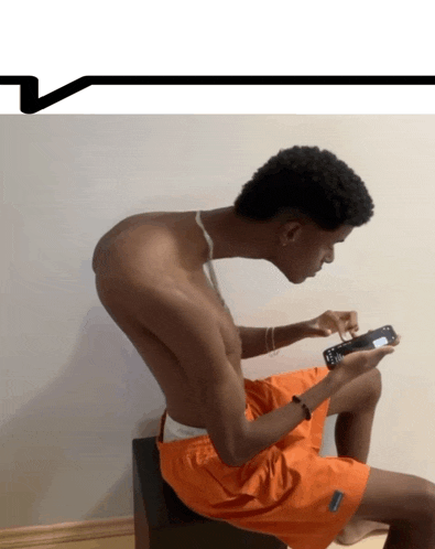 a shirtless man in orange shorts is sitting on a stool playing a video game