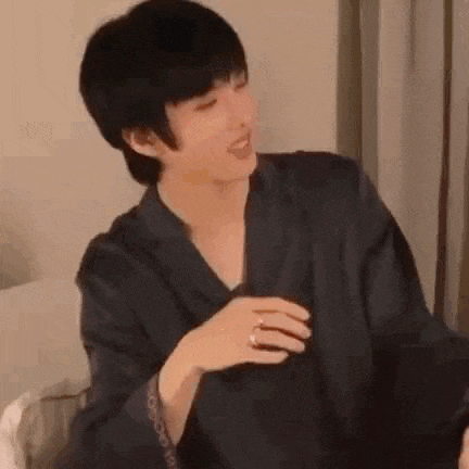 a young man is sitting on a bed wearing a black robe and a ring on his finger .