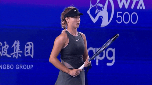 a woman holds a tennis racquet in front of a wta 500 sign