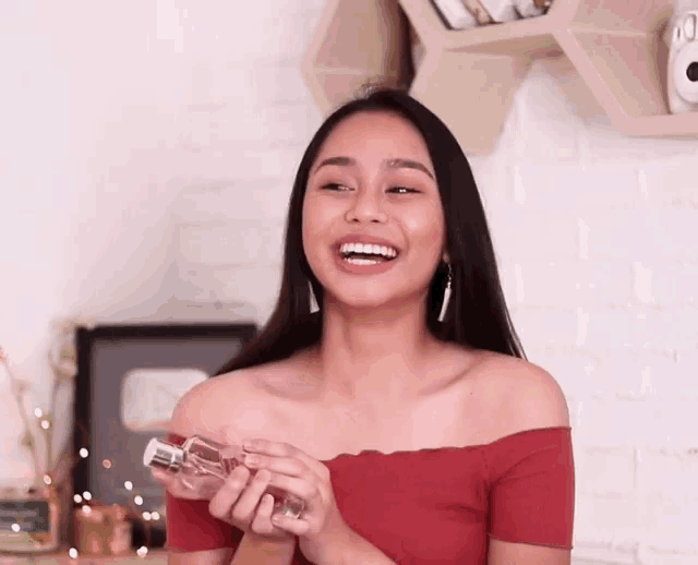 a woman is holding a bottle of perfume in her hands and smiling .