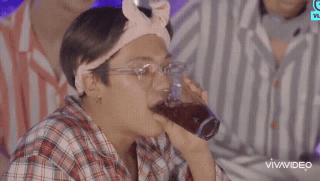 a man wearing glasses and a headband drinking from a glass .
