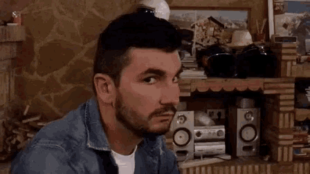 a man with a beard is sitting at a table in front of a stereo .
