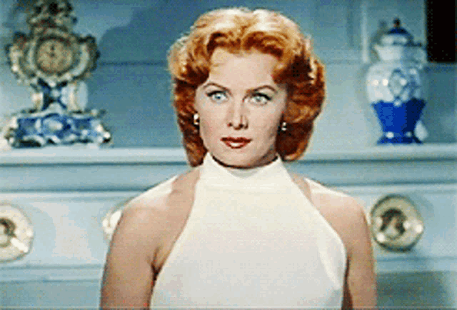 a woman in a white dress is standing in front of a fireplace