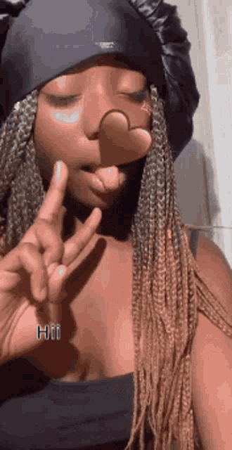 a woman wearing a hat and braids is making a peace sign