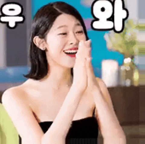 a woman in a black dress is smiling and clapping her hands in front of her face .