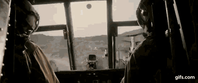 a couple of men are sitting in a cockpit of a helicopter looking out the window .