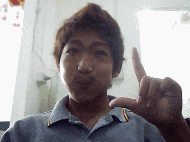 a man in a gray shirt is making a peace sign with his left hand