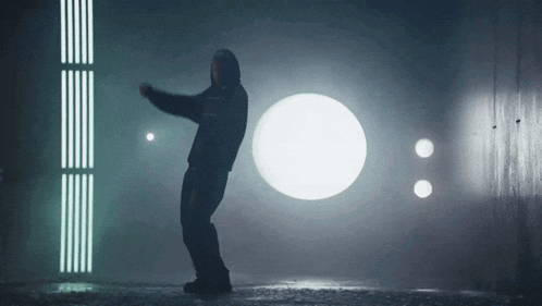 a man in a hooded jacket is dancing in a dark room with a circle in the background .