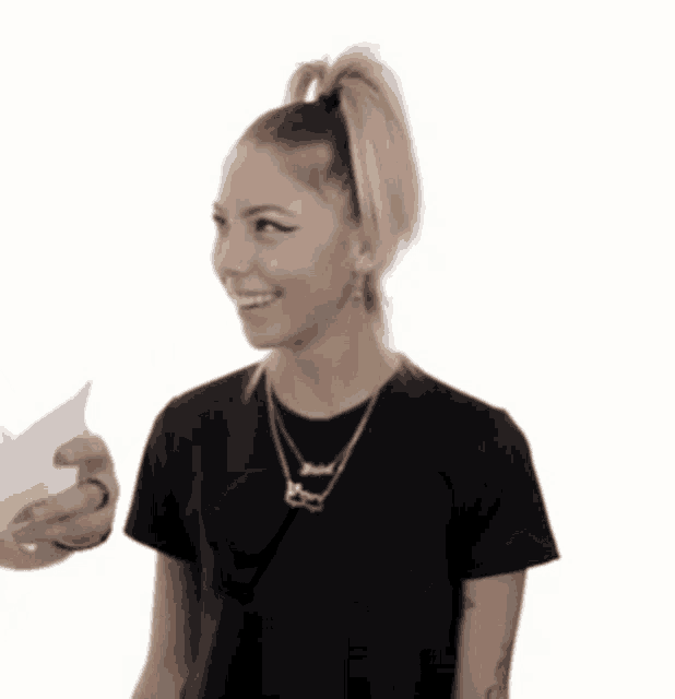 a woman in a black shirt is smiling while holding a piece of paper in her hand ..