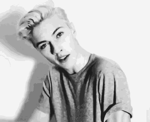 a black and white photo of a young man with short blonde hair wearing a gray t-shirt .