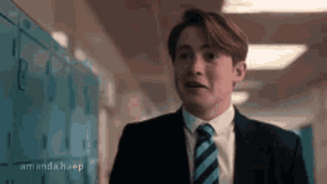 a young man in a suit and tie is walking down a hallway .