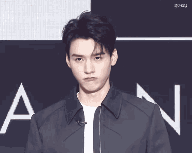 a young man is making a funny face while wearing a black jacket and tie .