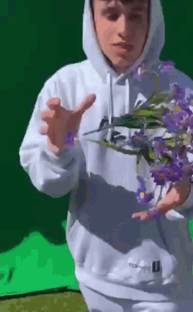 a man in a white hoodie is holding a bunch of purple flowers .