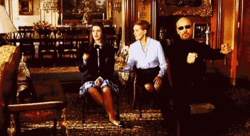 a man in sunglasses stands between two women sitting in chairs in a room
