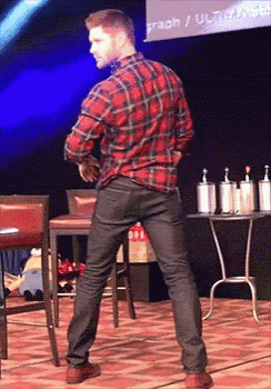 a man in a plaid shirt is standing on a stage with his hands behind his back