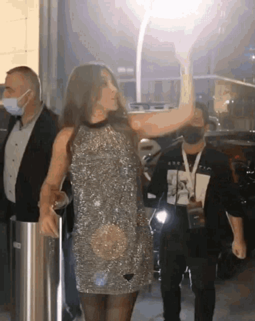 a woman in a sequined dress is being escorted by a man wearing a black mask