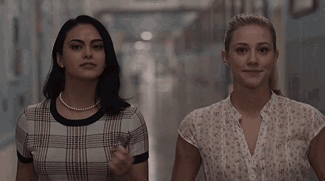 two women are walking down a hallway and talking to each other