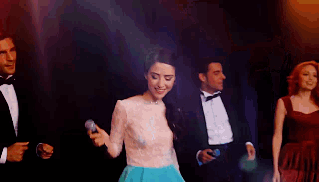 a woman in a blue dress sings into a microphone in front of a group of people in tuxedos