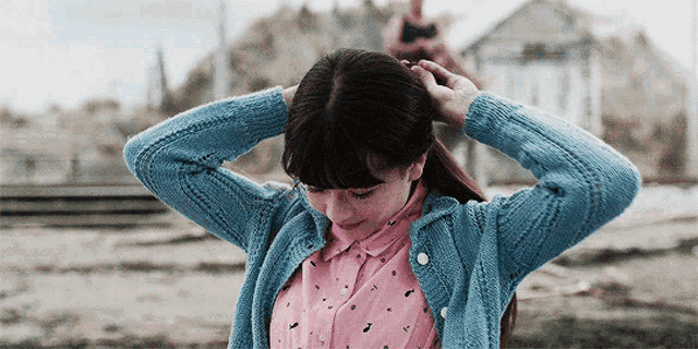 a girl in a blue sweater and pink shirt holds her hair up