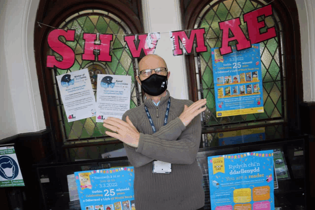 a man wearing a face mask stands in front of a sign that says shaw mae