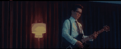 a man in a white shirt and tie is playing a guitar in a dark room .