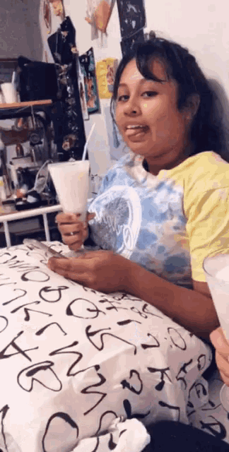 a girl is sitting on a bed holding a cup of milkshake