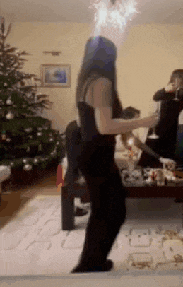 a woman is dancing in a living room with a christmas tree in the background