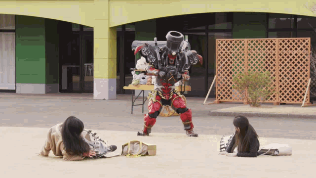 a man in a robot costume is standing in front of two girls laying on the ground