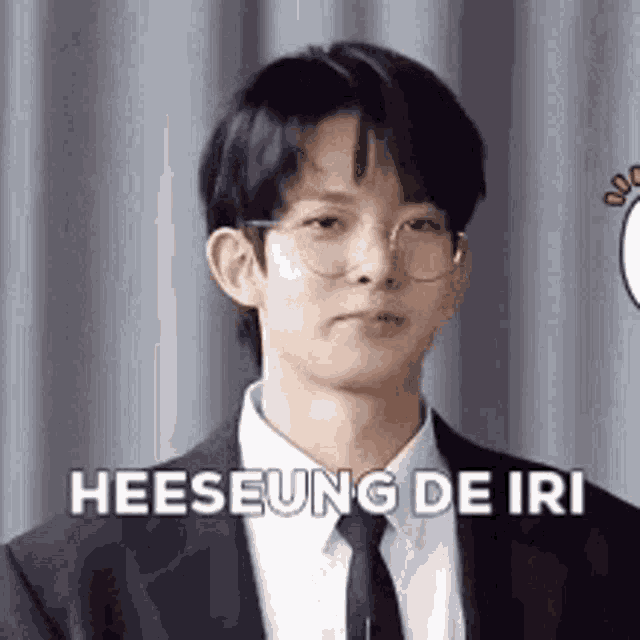 a young man in a suit and tie is wearing glasses and says heeseung de iri .