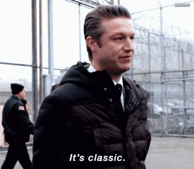 a man in a suit and tie says it 's classic in front of a fence