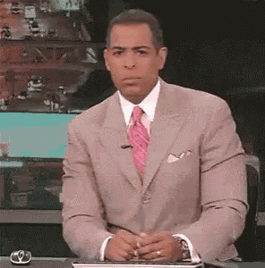 a man in a suit and tie is sitting at a desk with his hands folded in front of him .