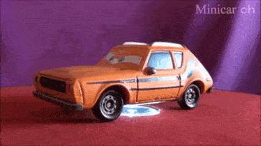 a toy car is sitting on a red surface with the words minicar ch written on the bottom