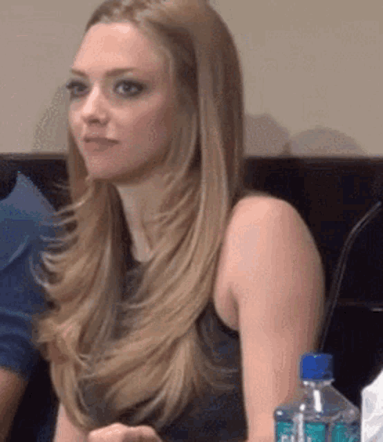 a woman with long blonde hair is sitting in a chair with a bottle of water in front of her .