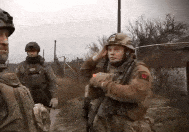 a group of soldiers are standing in a field and one of them is wearing a helmet with the letter r on it