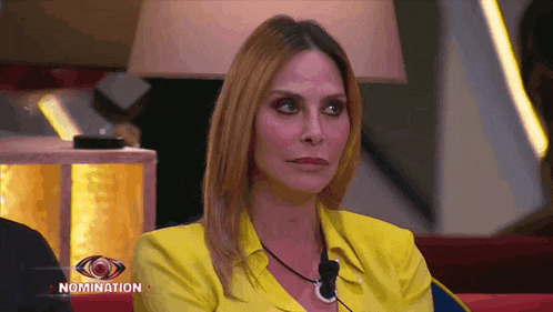 a woman wearing a yellow shirt is sitting in front of a screen that says nomination