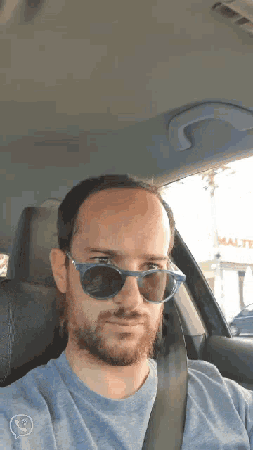 a man wearing sunglasses is sitting in a car in front of a malta sign
