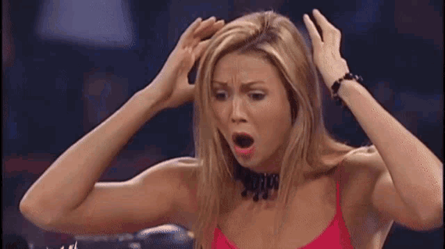 a woman in a red tank top is holding her head with her hands .