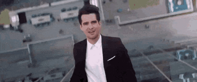 a man in a suit and white shirt is standing in front of a stadium .