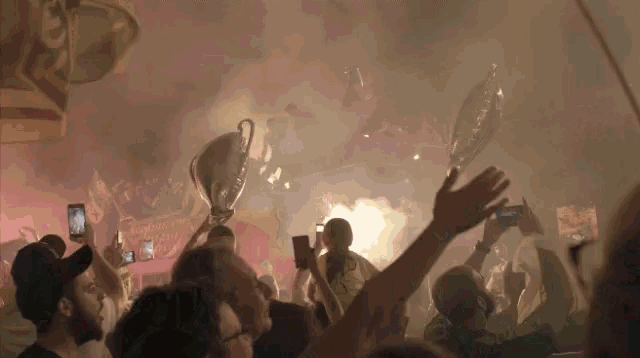 a crowd of people holding up trophies and balloons with smoke coming out of them