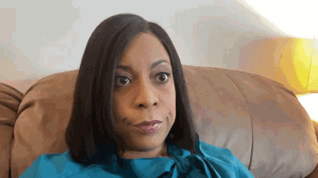 a woman in a blue shirt sits on a brown leather couch