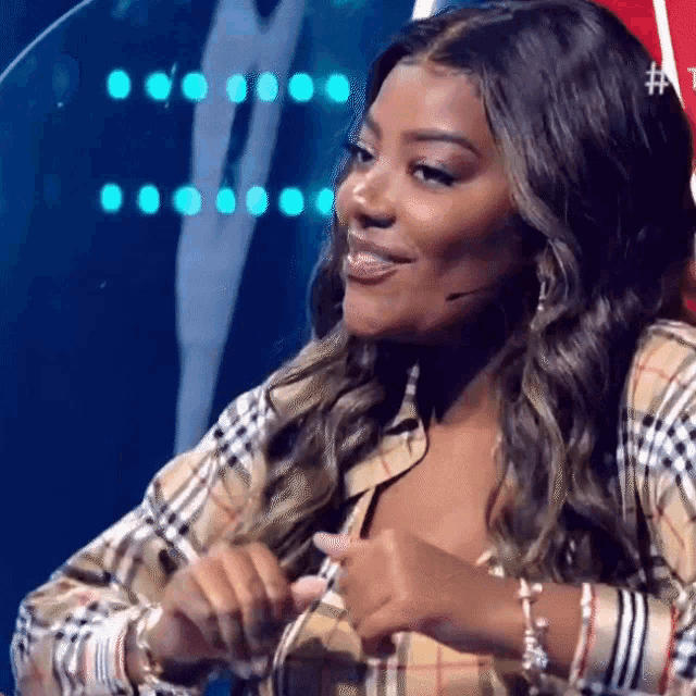 a woman wearing a plaid shirt and bracelets is sitting in front of a microphone and smiling .