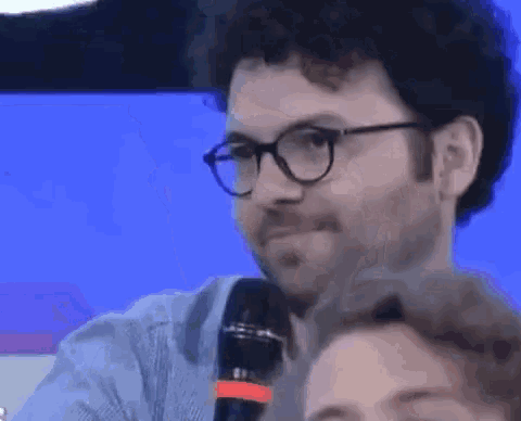 a man with glasses and a beard is talking into a microphone