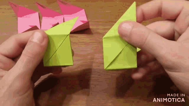a person is holding a green and pink origami triangle with the words made in animotica below them