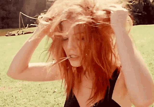 a woman with red hair is holding her hair in a field