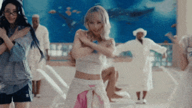 a group of women are dancing in a room with a blue wall behind them
