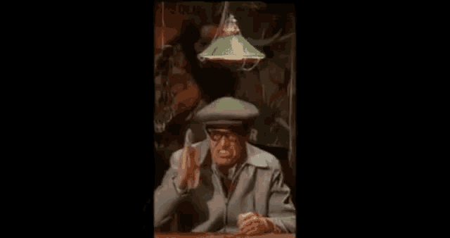 a man is sitting at a table with a green lamp hanging from the ceiling and talking .